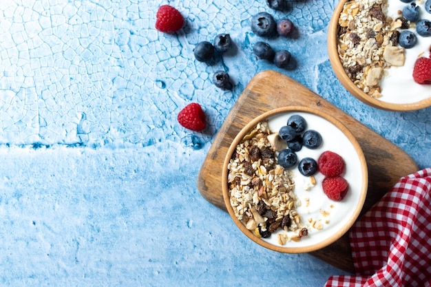 Yogurt con frutti di bosco e muesli per colazione in una ciotola su sfondo blu