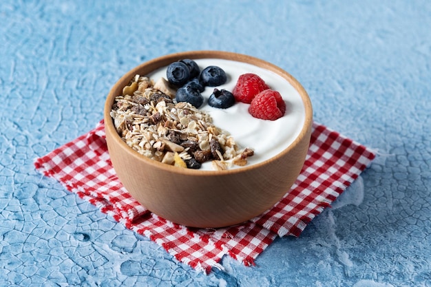 Yogurt with berries and muesli for breakfast in bowl on lbue background