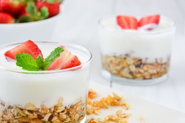 Yogurt with cereals and strawberries on white wooden table