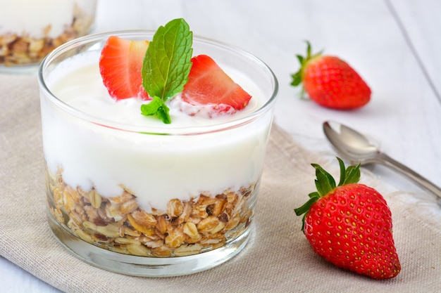 Yogurt with cereals and strawberries on white wooden table