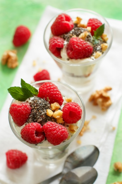 Yogurt with chia seeds, walnuts, mint and raspberries on green close up
