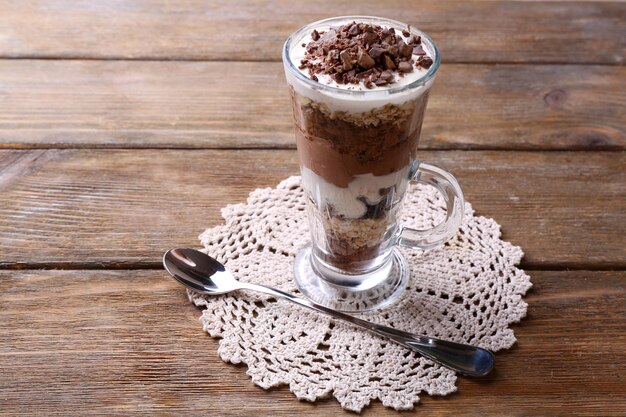 Yogurt with chocolate cream chopped chocolate and muesli served in glass on wooden background