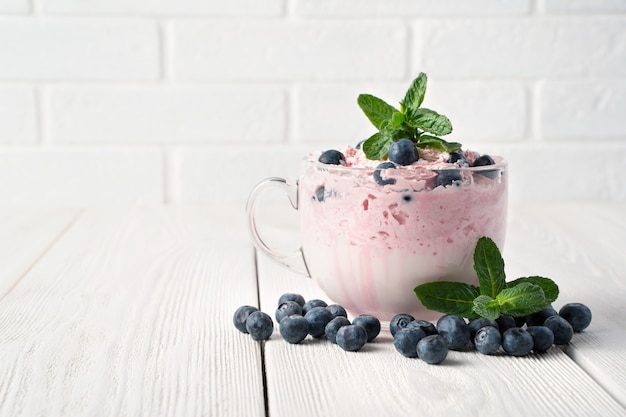 Yogurt with cream and berries on a white table.