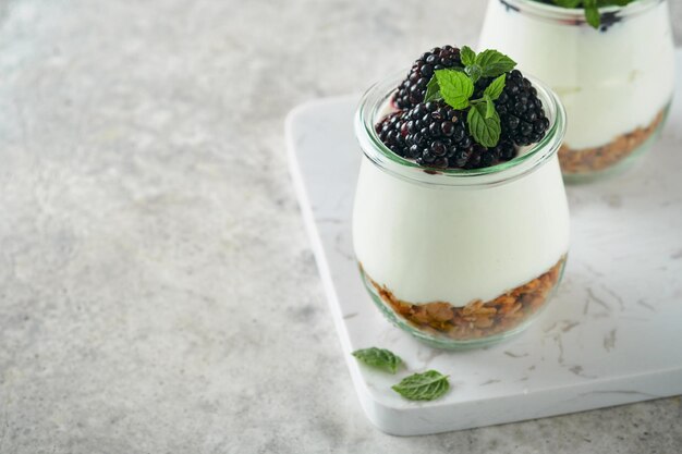 Yogurt with granola blackberry berry fruits and muesli served in glass jar on gray concrete table background Healthy breakfast concept Healthy food for breakfast top view