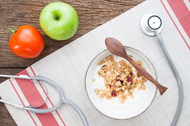 Yogurt with granola in a bowl and stethoscope on wooden table