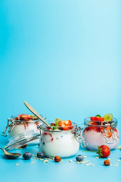 파란색 배경에 있는 항아리에 그라놀라 신선한 딸기와 견과류를 넣은 요구르트 건강한 아침 식사와 우유 ...