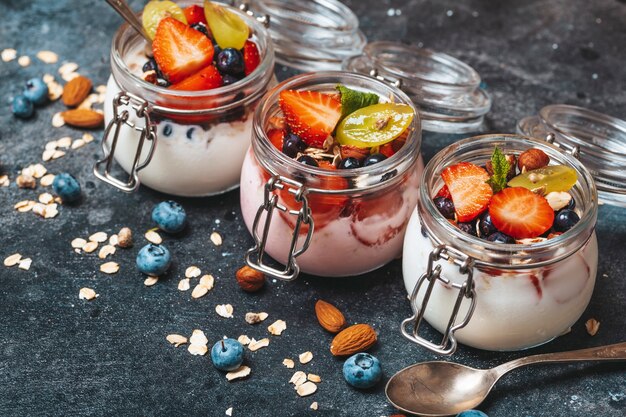 Yogurt with granola fresh berries and nuts in a jar on a dark background healthy breakfast and desse...