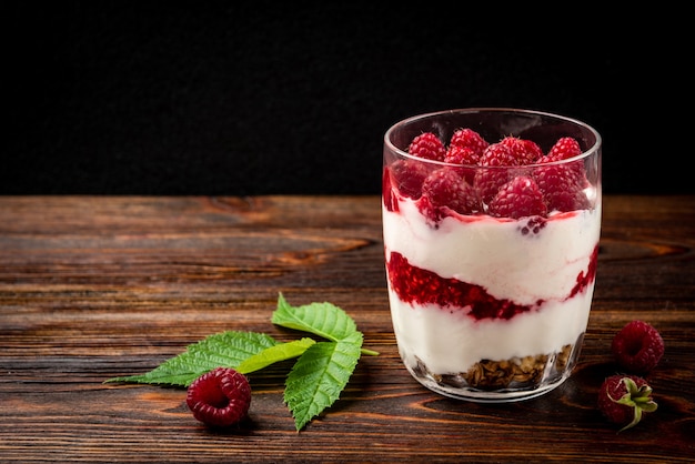 Yogurt with granola, raspberry and raspberry jam on dark wooden table.