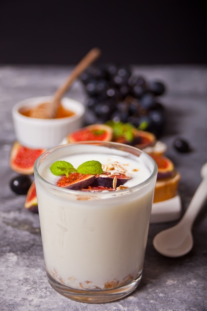 Yogurt with muesli and fig fruit in a glass, sandwich with cream cheese, figs and honey on the concrete . Healthy food . Autumn harvest.