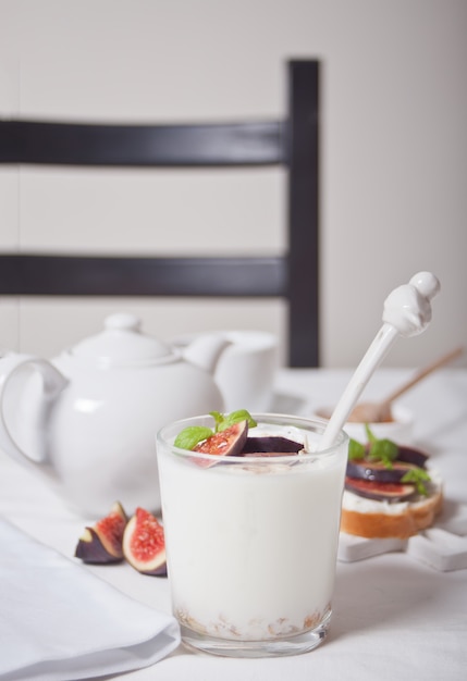 Yogurt with muesli and fig fruit in a glass, sandwich with cream cheese, figs and honey on the white . Healthy food .