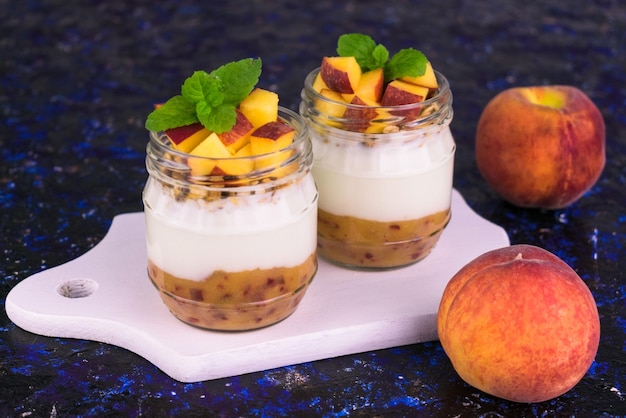 Yogurt with peach and granola in jars on a blue background