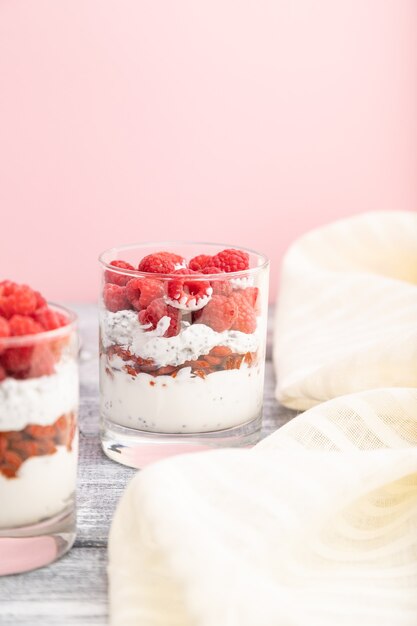 Йогурт с малиной, ягодами годжи и семенами чиа в стакане на серо-розовой поверхности и льняной ткани