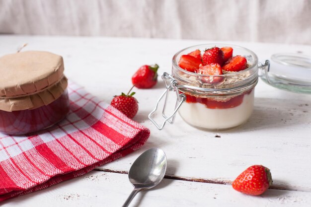 Yogurt with ripe fresh strawberries and banana and strawberry jam in glass jar on the wooden table