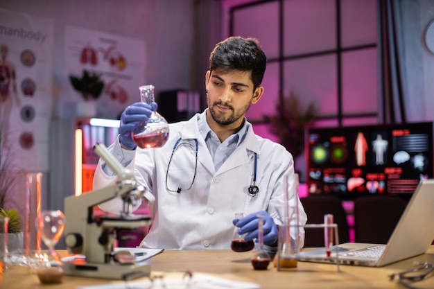 Yong indian male scientist working with test tubes wearing lab coat working in laboratory