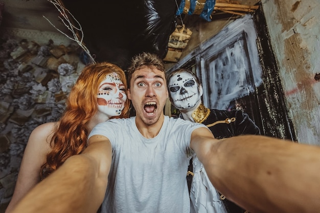 Photo yong man making selphie with actors man and woman in halloween costume and makeup in studio with mystical interior.