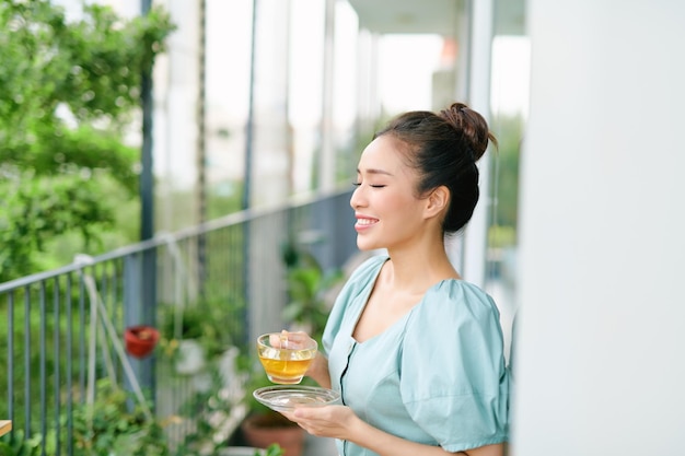 Yong meisje met kopje thee staande op het balkon in de ochtend