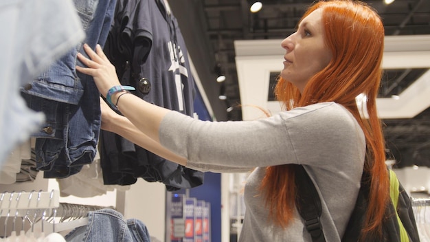 Yong positieve vrouw kiest een jurk in de dameskledingwinkel, close-up