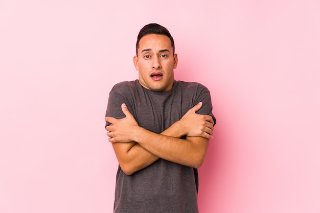 Yooung latin man posing in a pink wallgoing cold due to low temperature or a sickness.