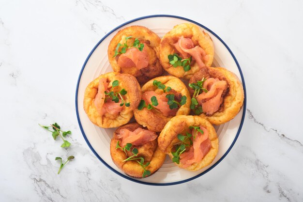 Yorkshire pudding tradizionale inglese yorkshire pudding con salmone e ravanello microgreens contorno su piastra bianca e sfondo grigio chiaro tavolo vista dall'alto