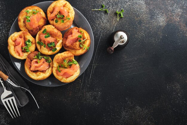 Yorkshire pudding Traditionele Engelse Yorkshire pudding met zalm en radijs microgreens bijgerecht op donkergrijze plaat en donkere achtergrond tafel Bovenaanzicht