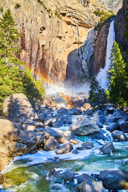 Yosemite Falls with frosty waters over rocks and rainbow