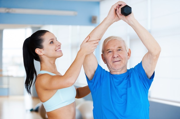 You are making great progress! Confident female physical therapist working with senior man in health club