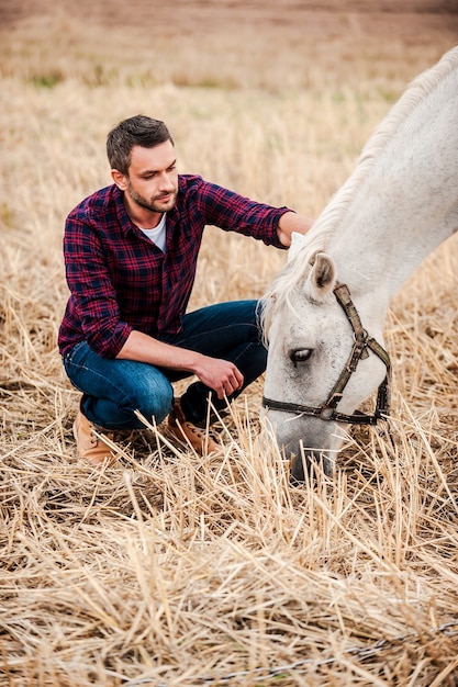 You are so beautiful! Side view of young farmer touching horse while sitting outdoors