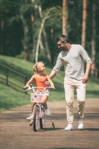 You can do it! Full length of cheerful father teaching his daughter to ride a bicycle in park