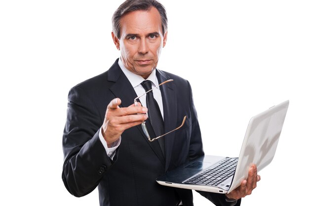 You can trust me! confident mature man in formalwear holding laptop and pointing you while standing isolated on white background