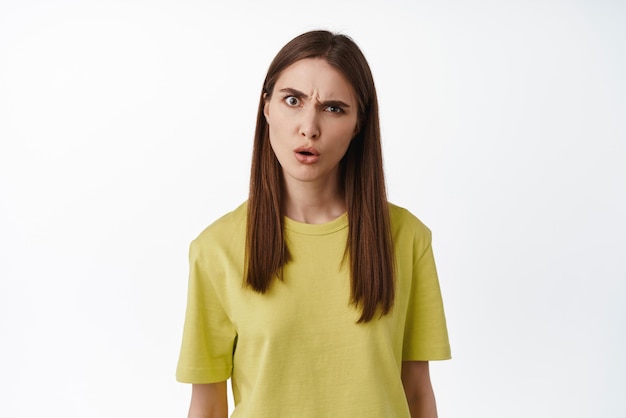 You say what Confused and annoyed woman making creepy strange face grimacing and raising eyebrow suspicious staring at camera puzzled standing against white background