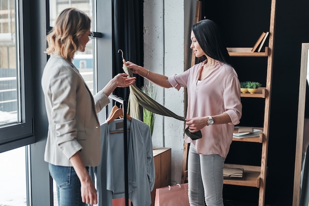 you should try it on. beautiful young woman helping to choose clothes to her 