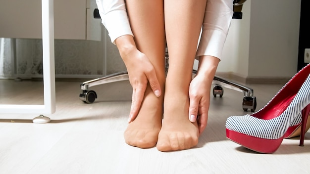 yougn woman feeling pain in legs and feet after hard working day in office.