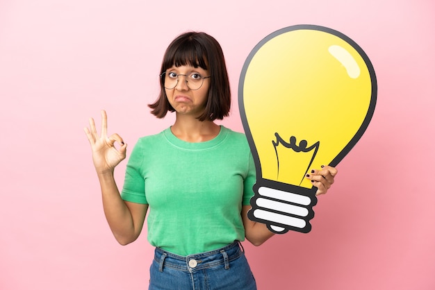 Photo youing woman holding a bulb icon and doing ok sign