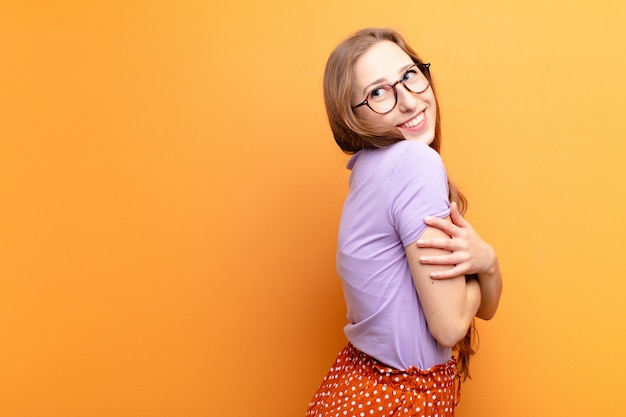 Yound blonde woman smiling gleefully, feeling happy, satisfied and relaxed, with crossed arms and looking to the side