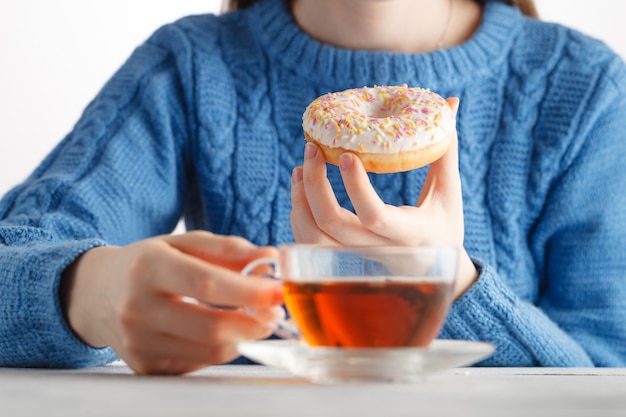 Photo younf woman drink tea and hold donut in hand