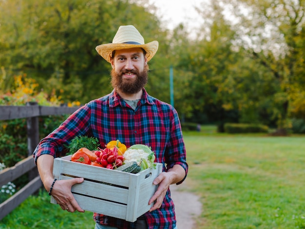 상자 30-35 세 젊은 수염 남자 남성 농부 모자 상자 신선한 생태 야채 정원 일몰.