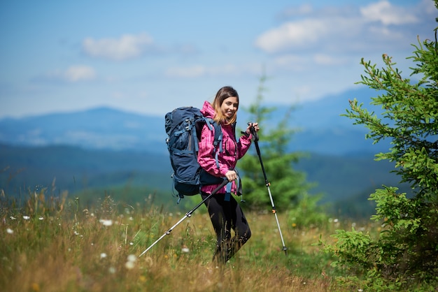 배낭과 트레킹 스틱, 산에서 트레킹, 화창한 날을 즐기는 젊은 활성 여성 산악인. 활동적인 라이프 스타일의 개념