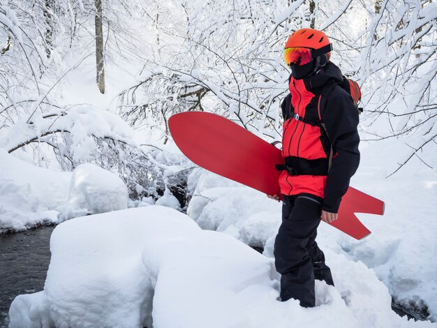 冬の森で雪の中に立っているツバメの尾のスノーボードを持つ若いアクティブな男