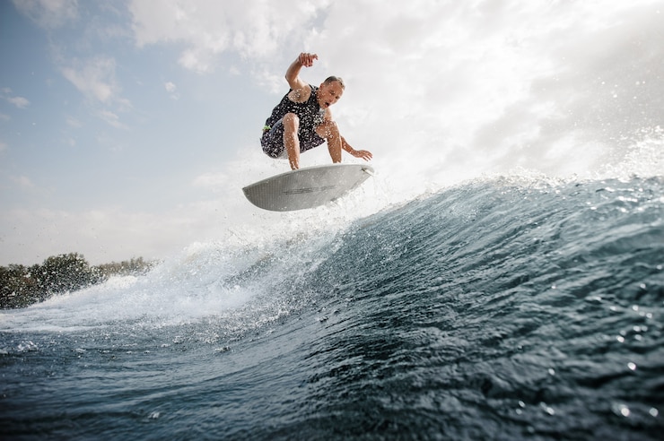 Photo young active man jumping on the white wakeboard down the blue water against grey sky