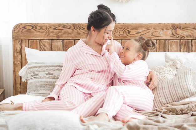 Young active mother and her little daughter having fun together at home in the bedroom wearing pajamas