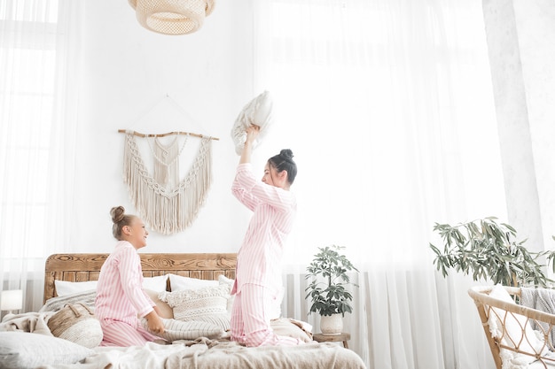 Young active mother and her little daughter having fun together at home in the bedroom wearing pajamas