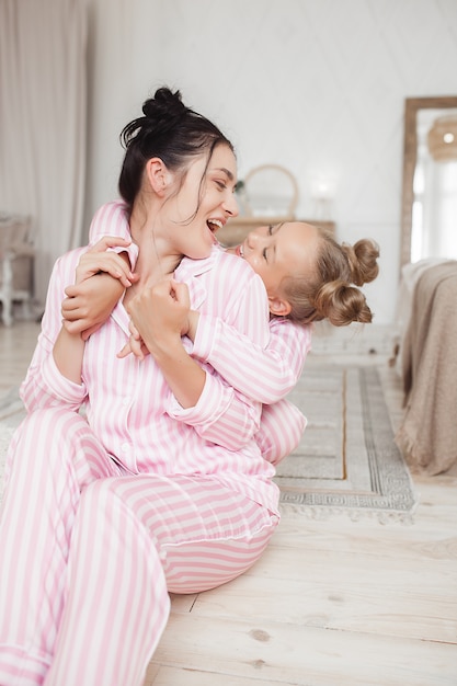 Young active mother and her little daughter having fun together at home in the bedroom wearing pajamas