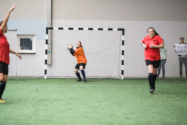 Молодая активная спортсменка собирается бросить футбольный мяч другому игроку своей команды, стоя у ворот во время игры