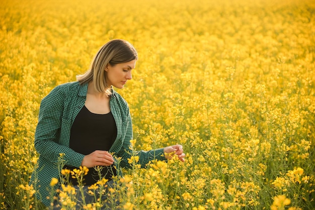 Young adorable woman farmer investigate rapeseed crop farmland traditional side view of a female far