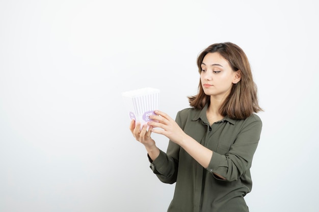 Giovane donna adorabile guardando la scatola di popcorn su bianco. foto di alta qualità