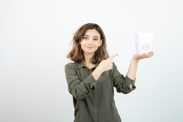 Young adorable woman pointing at popcorn box and posing. High quality photo