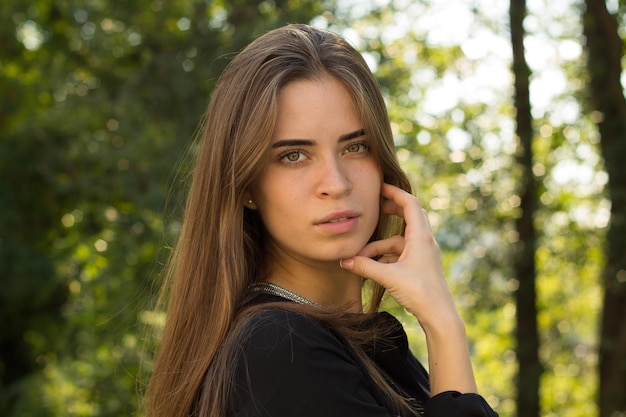 Young adoreable woman with long brown hair in black blouse and silver necklace standing back