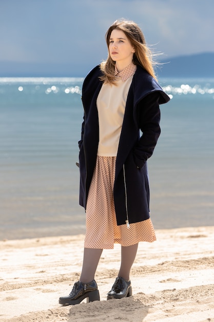 A young adult beautiful girl stands on the shore against the backdrop of an approaching cloud with rain