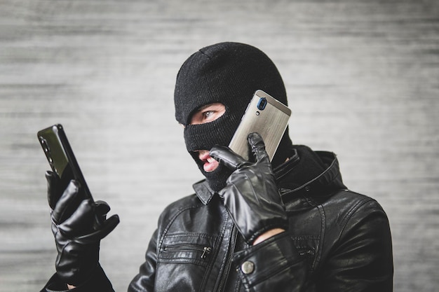 Young adult in black clothes with hidden face Illintended fraudster uses mobile Fraudster calls Scam Mobile racket Hacker hijacks by phone Cellphone account fraud