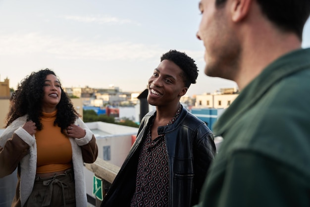 young adult black male smiling whilst amongst multicultural friends in the city on a rooftop terrace